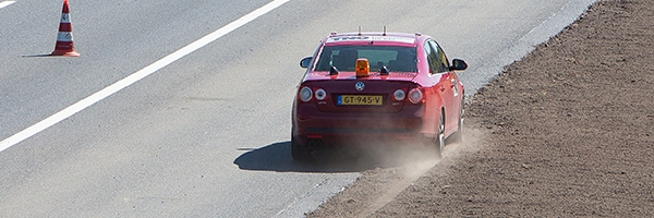 Een rode volkswagen van TNO test de rand van een weg